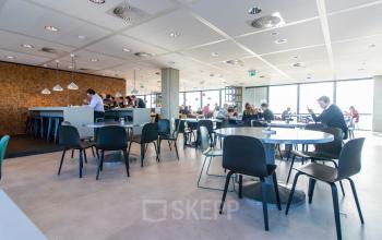 Modern office space in Amsterdam East at Piet Heinkade 55 with professionals engaged in work discussions at tables, highlighting a bright and collaborative environment ideal for office space rental.