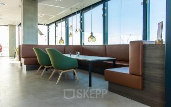 Modern office lounge area with large windows, green chairs, and brown leather seating at Piet Heinkade 55, ideal for an office space rental in Amsterdam East.