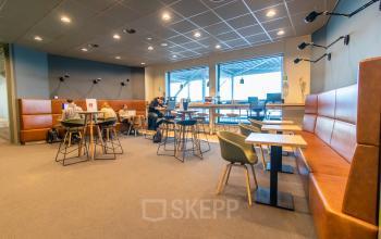 Modern office space rental at Piet Heinkade 55 in Amsterdam East, featuring stylish furniture and individuals engaged in meetings and work discussions.