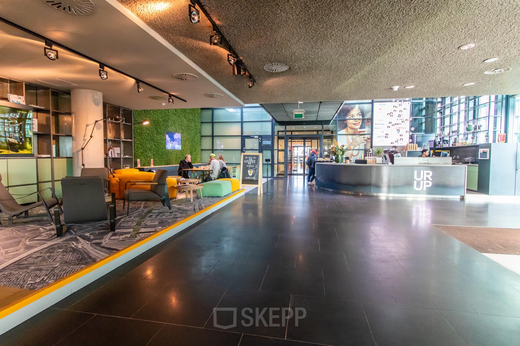 Spacious office lobby at Piet Heinkade 55, Amsterdam East, featuring modern furnishings and people engaging in business conversations, ideal for office space rental.