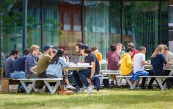 Groups of people engaged in conversations at picnic tables outside an office building at Science Park 301, Amsterdam East. A vibrant setting ideal for networking and collaboration.