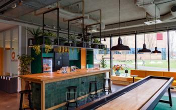 Modern office space at Science Park 301, Amsterdam East featuring a stylish furnished interior with a wooden bar, green tiles, and seating area perfect for office space rental. Large windows offer natural light.
