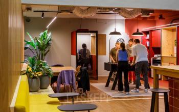 Modern furnished office space rental at Science Park 301, Amsterdam East, featuring a stylish lounge area with indoor plants and a group engaged in a team collaboration activity around a foosball table.