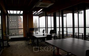 Office space at KNSM-Laan 171, Amsterdam East, featuring large windows with city views and several desks, available for rent.