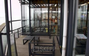 Outdoor view of a modern office space for rent at KNSM-Laan 171, Amsterdam East, featuring stylish black seating and large glass windows.