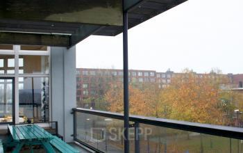 A covered outdoor terrace with seating, providing a view of the neighboring buildings in Amsterdam East. Suitable for breaks or informal meetings.