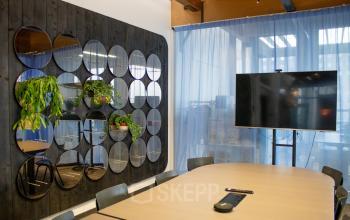 Modern office to rent at KNSM-Laan 171, Amsterdam East, featuring a meeting room with a large table, chairs, decorative plants, and a wall-mounted screen.