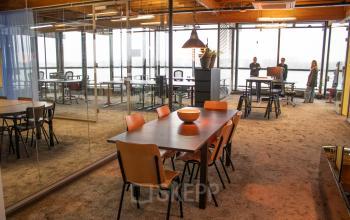 Modern office space for rent at KNSM-Laan 171, Amsterdam East, with furnished workstations and a meeting table. People are discussing a project.