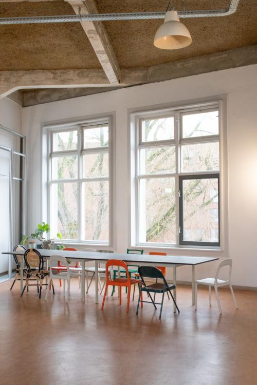 Bright office space with large windows and a central table with chairs, perfect for office space rental in Amsterdam East.