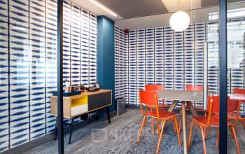 Bright conference room with blue patterned walls, orange chairs, wooden table, and decorative desk at Weesperstraat 61 in Amsterdam Oost, ideal for office space rental.