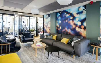 Modern office lounge at Weesperstraat 61, Amsterdam East, featuring a comfortable seating area with colorful decor and view into adjacent workspaces.