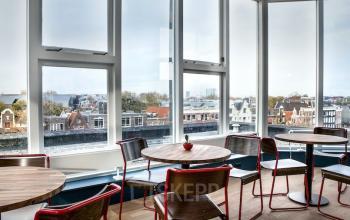 Bright office to rent at Weesperstraat 61, Amsterdam East, featuring large windows, modern furniture, and a city view.