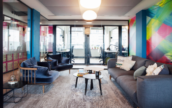 Bright, colorful office lounge at Weesperstraat 61 in Amsterdam Oost with cozy seating and vibrant wall art, leading to glass-walled workspaces.