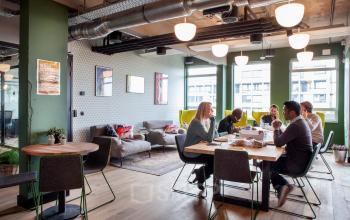 Modern furnished office to rent at Weesperstraat 61, Amsterdam East, with a cozy lounge area and team collaborating at a large table.