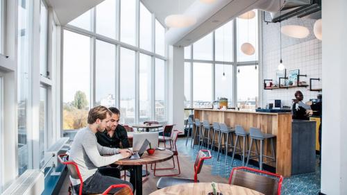 Bright office space at Weesperstraat 61, Amsterdam East, with large windows, modern furniture, and a bar area; two people working on a laptop.