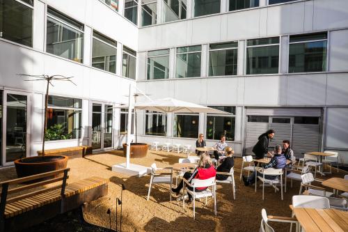 Outdoor seating area at the Apollolaan 151 office in Amsterdam Old South. Several people engaged in business discussions, highlighting the space's versatility for office space rental.