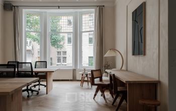 Bright office space with wooden desks and chairs near a large window on Jacob Obrechtstraat 56, ideal for office space rental in Amsterdam Old South.