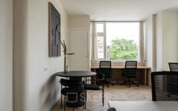 Office space with two desks near a window and a small round table with chairs, available for rent in Amsterdam Old South.