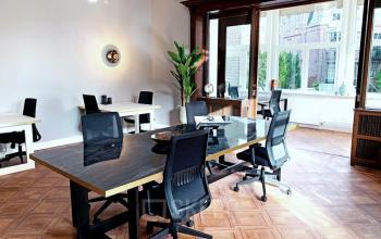 Bright office space in Amsterdam Old South at Emmalaan 7-9, featuring modern desks and chairs available for rent. Large windows allow natural light, ideal for productive work environments.