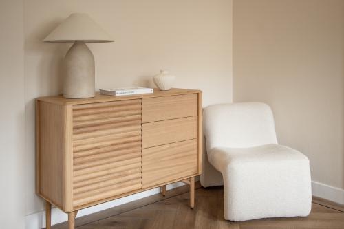 A cozy corner in an Amsterdam Old South office to rent, featuring a stylish wooden sideboard, a modern lamp, and a comfortable chair on a parquet floor.