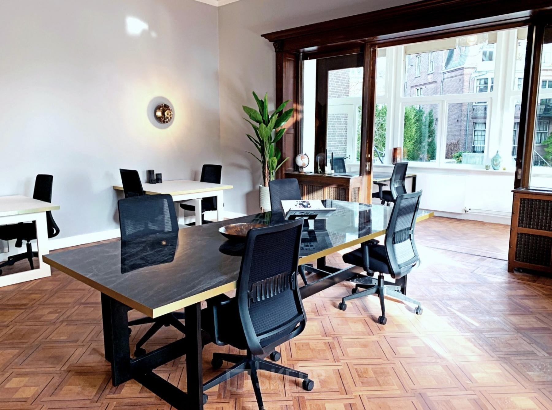 Bright office space in Amsterdam Old South at Emmalaan 7-9, featuring modern desks and chairs available for rent. Large windows allow natural light, ideal for productive work environments.