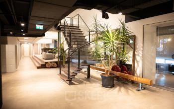 Modern office interior at Olympisch Stadion 24-28, Amsterdam Old South, featuring open space with plants, staircase, and relaxation area in the background.