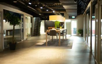Open floor plan office space with modern furnishings at Olympisch Stadion 24-28, Amsterdam Old South. Features a long table, chairs, and plants under ample lighting.