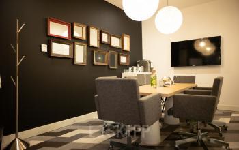 Modern office space rental at Olympisch Stadion 24-28, Amsterdam Old South, featuring a meeting room with a wooden table, grey chairs, a black accent wall with framed mirrors, and a wall-mounted TV.
