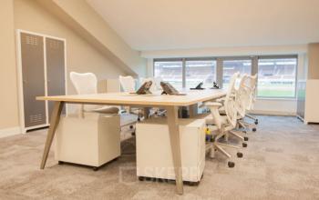 Modern office space at Olympisch Stadion 24-28, Amsterdam Old South, featuring a large work table, ergonomic chairs, and lockers with a view overlooking the stadium.
