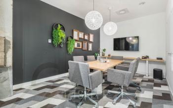 A modern conference room with a wooden table, grey chairs, wall-mounted TV, and decorative plants at Olympisch Stadion 24-28 in Amsterdam Old South, available for office space rental.