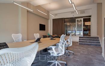 Office space rental at Olympisch Stadion 24-28, Amsterdam Old South. Features modern workstations, ergonomic chairs, large windows, and a conference area in the background.