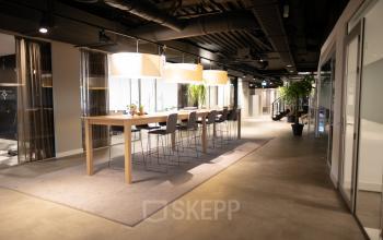 Modern office with a communal work area, featuring long wooden tables, high chairs, and plants at Olympisch Stadion 24-28, Amsterdam Old South. Ideal for those looking for office space rental.