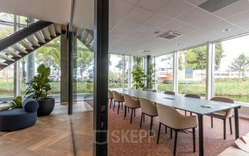 Bright office space with a large conference table and seating at John M. Keynesplein 4-10, Amsterdam Riekerpolder, showcasing an inviting area for office space rental.