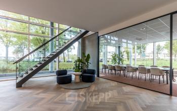 Spacious office reception in Amsterdam Riekerpolder, featuring a seating area with modern chairs and a conference room with tables and chairs, ideal for office space rental.