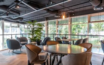 Modern furnished office space in Amsterdam Riekerpolder with round tables and chairs, featuring large windows for natural light and greenery, ideal for office space rental.