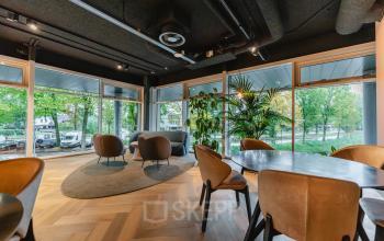 Modern office space with large windows, stylish seating, and wooden flooring at John M. Keynesplein 4-10, ideal for rent office space in Amsterdam Riekerpolder.
