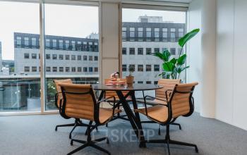 Bright office space with a round table and four chairs near large windows, located at John M. Keynesplein 4-10, an ideal spot for those seeking office space rental in Amsterdam Riekerpolder.