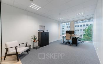 Furnished office space at John M. Keynesplein 4-10, Amsterdam Riekerpolder, featuring a desk, chairs, and cabinets near a large window with city views.