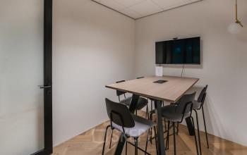 Modern office meeting space at John M. Keynesplein 4-10, Amsterdam Riekerpolder, featuring a table with chairs and a mounted screen for rent.