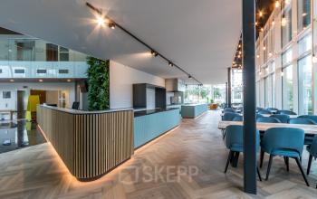 Spacious office interior in Amsterdam Riekerpolder with modern design, featuring large windows, wooden flooring, and stylish furnishings ideal for office space rental.