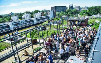 A bustling outdoor event at an Amsterdam Riekerpolder office space for rent, with professionals networking on a sunny day.