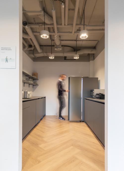 Modern office pantry at Teleportboulevard 120, Amsterdam Sloterdijk, featuring sleek cabinetry and a person opening a fridge. Ideal for office space rental with convenient amenities.