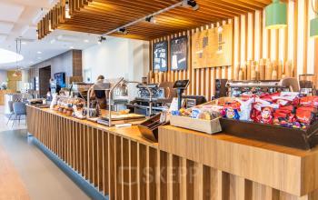 A welcoming pantry area at office space rental on Radarweg 29, Amsterdam Sloterdijk, featuring light wood decor and a variety of snacks for employees. A person is preparing coffee at a machine.