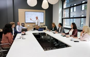 A team engaged in a meeting around a modern conference room table at Teleportboulevard 110, with large windows providing natural light in Amsterdam Sloterdijk. A perfect office space rental opportunity.