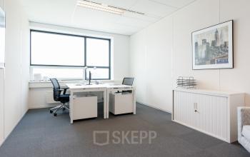 Bright and minimally furnished office space for rent at Teleportboulevard 110, Amsterdam Sloterdijk, featuring desks, chairs, and a large window.