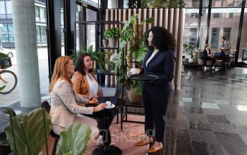Office space at Teleportboulevard 110 in Amsterdam Sloterdijk, featuring a lively work environment with people seated at tables, engaged in conversation, surrounded by plants and modern decor.