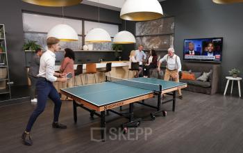 Lively office space at Teleportboulevard 110, Amsterdam Sloterdijk, featuring a ping pong table with people playing and others socializing in the background, ideal for office space rental.