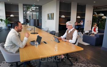 Professionals engage in discussions and work on laptops in a contemporary office space available for rent at Teleportboulevard 110, Amsterdam Sloterdijk.