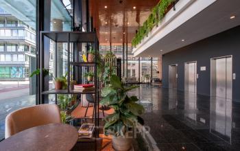 Modern office space available for rent at Teleportboulevard 110, Amsterdam Sloterdijk, featuring vibrant greenery and stylish furnishings in a bright lobby area.