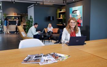 Modern office space at Teleportboulevard 110, Amsterdam Sloterdijk, featuring a casual workspace with people working on laptops and discussing business. Ideal for those seeking office space rental.